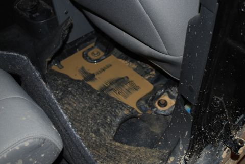 2008 Jeep Wrangler - Interior floor area behind a seat with the carpet pulled back, revealing a tan/gold painted metal floor pan with exposed mounting bolts and…