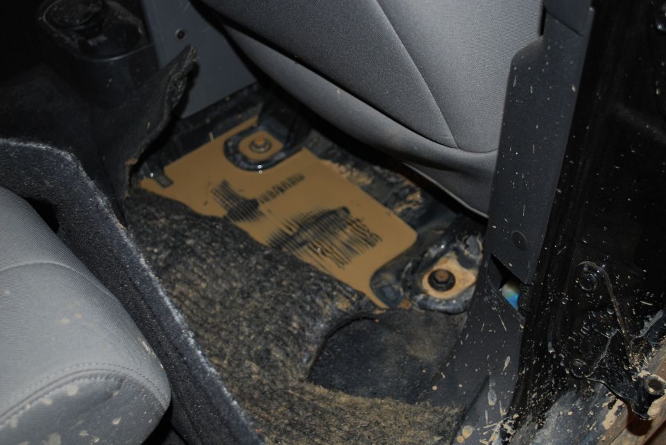 Jeep interior floor pan exposed with carpet folded back, showing bolts and debris