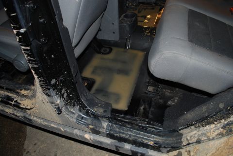 2008 Jeep Wrangler - Interior of a Jeep Wrangler with the carpet removed, showing the bare black floor pan, molded plastic drain plugs, gray cloth seats and mud…