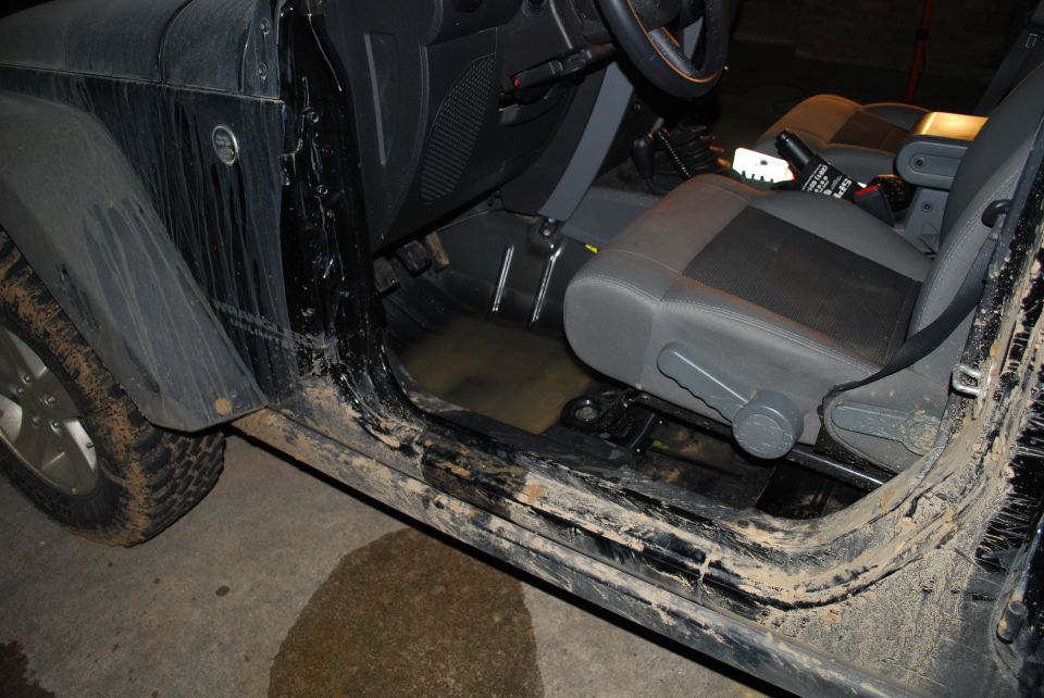 Muddy Jeep Wrangler interior with water pooled on the driver's floor pan, doors removed