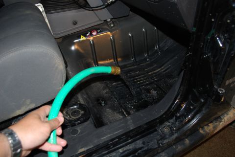 2008 Jeep Wrangler - Interior floor of a Jeep with carpet and seat removed, exposing the bare metal floor pan; a green garden hose with a brass fitting is being…