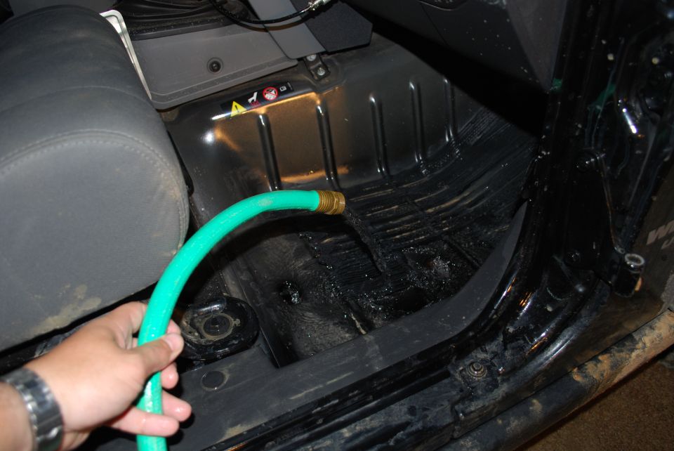 Green hose held over bare Jeep floor pan with seat and carpet removed