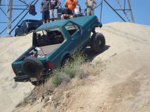 1986 Ford Bronco - A modified green SUV navigates a steep sandy hill with onlookers observing the off-road action.