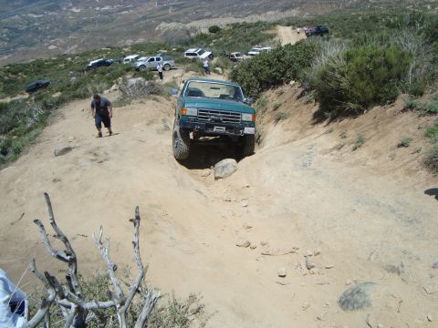 1986 Ford Bronco - A group of off-road vehicles tackle a challenging dirt path on a sunny day.