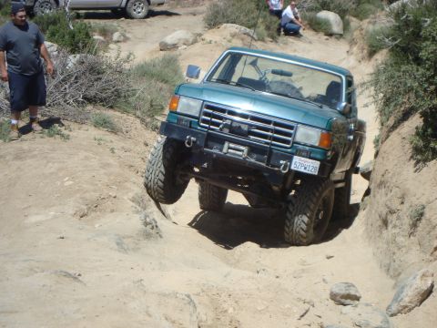 1986 Ford Bronco - This teal 1987 Ford F-150 is navigating a challenging off-road trail with a rocky incline.