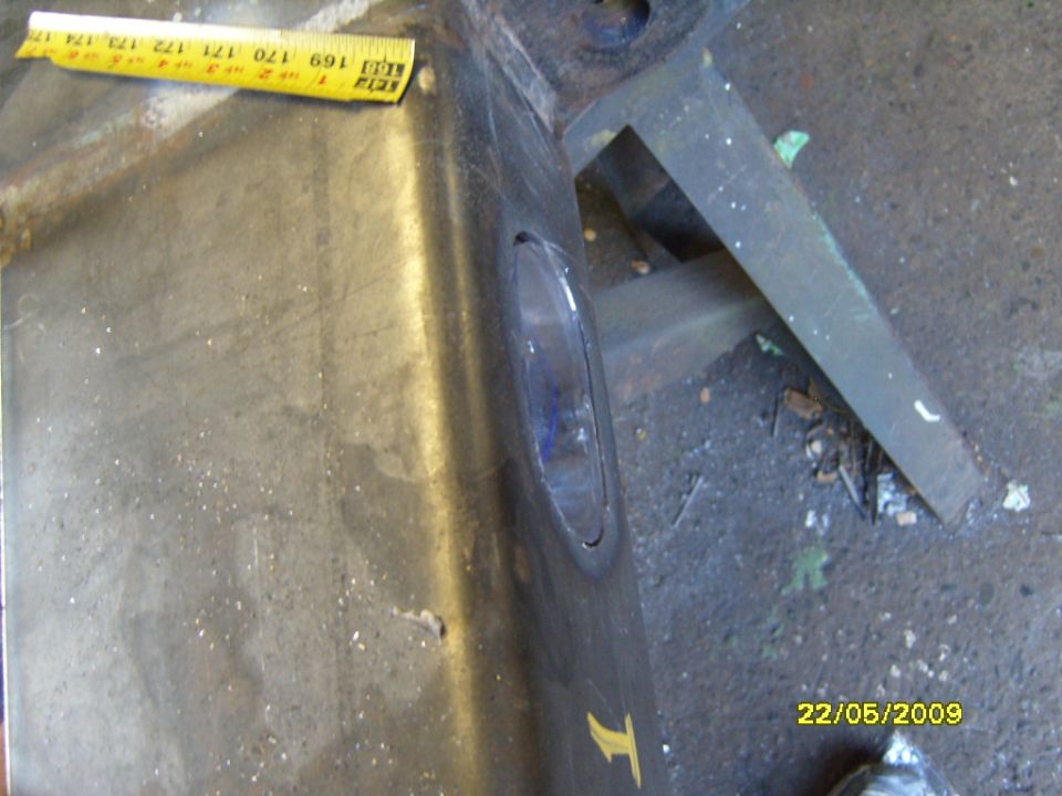 Close-up of a dark-colored vehicle bumper section with a yellow measuring tape. A yellow 'T' symbol is visible