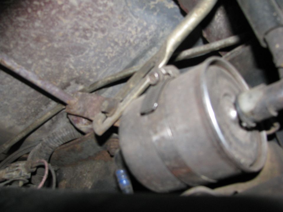 Underbody view of an inline fuel filter with metal clip and fuel lines under a 1986 Ford Bronco