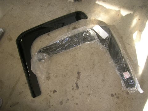 1996 Ford Bronco - Two black plastic fender flares are shown on a concrete surface, one loose and the other still in its original packaging.