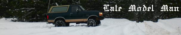 Dark green and tan Ford Bronco with large tires driving in snow