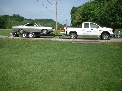 1971 Ford Torino - A silver coupe is transported on a trailer, pulled by a white pickup truck on a sunny day.