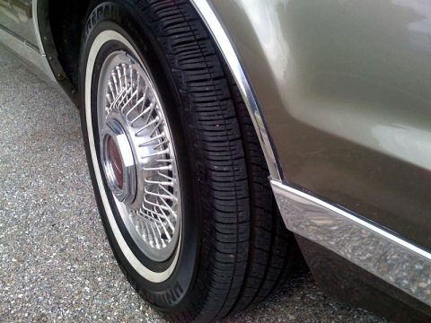 1987 Lincoln Mark VII - A close-up view of a car's wheel, tire, and fender trim, showing a wire-spoke hubcap and whitewall tire.
