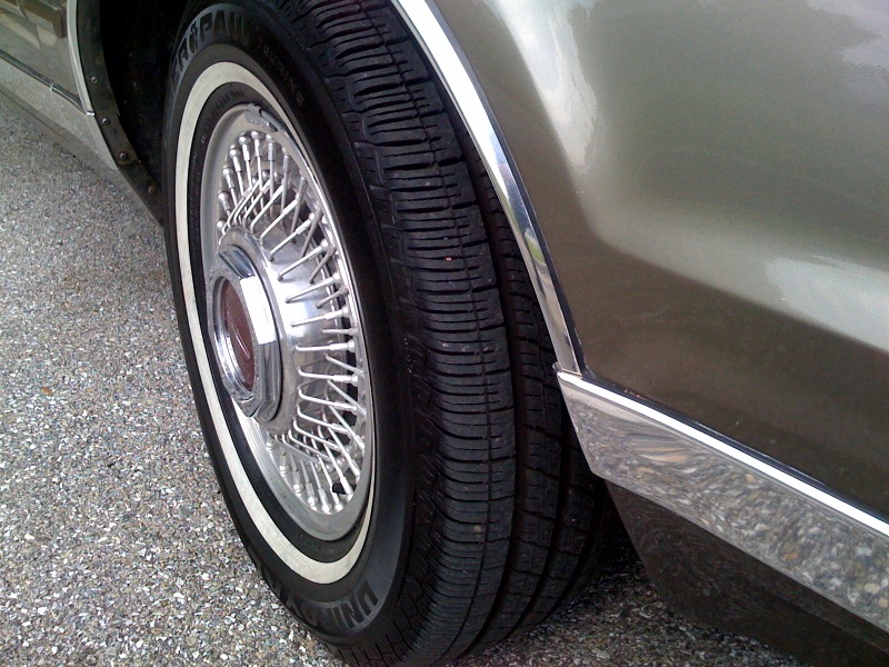 Close-up of a wire-spoke hubcap on a car with a whitewall tire and chrome trim
