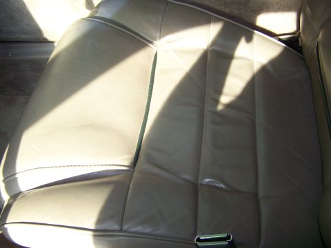 1987 Lincoln Mark VII - The interior of a car shows a tan leather seat with prominent stitching and sunlight casting shadows.