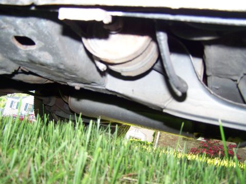 1987 Lincoln Mark VII - A close-up view of the undercarriage of a vehicle, with grass and a house in the background.