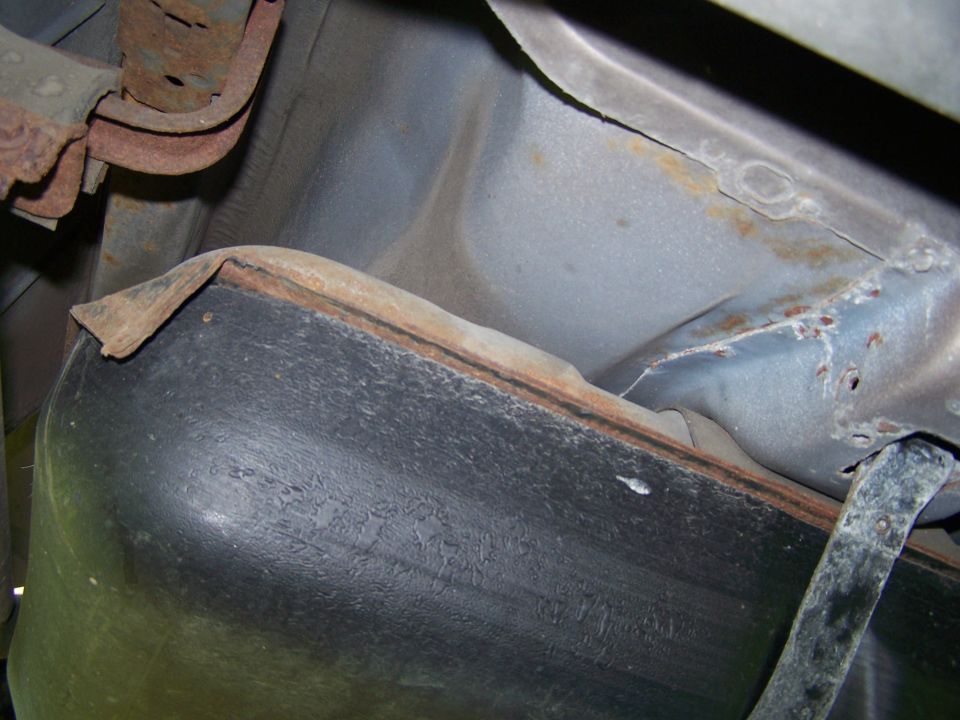 Underside view of a vehicle showing a fuel tank and rusted suspension components. SUPERMOTORS.NET logo visible