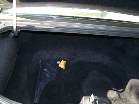 1987 Lincoln Mark VII - The interior of a car trunk is visible, showing dark carpeting and a black pouch with a yellow tag.