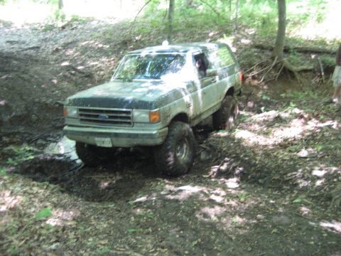1991 Ford Bronco - A Ford Bronco navigates a challenging off-road trail in a forest setting.