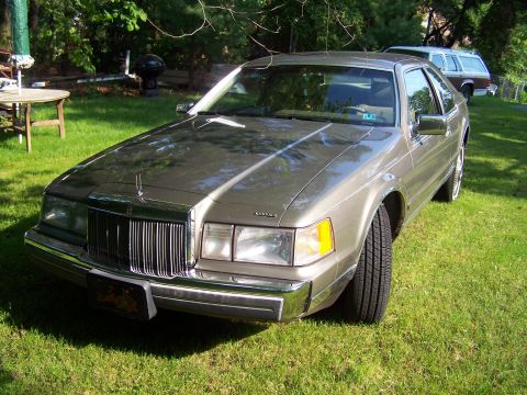 1987 Lincoln Mark VII - A brown Lincoln Mark VII coupe sits on a grassy lawn with a station wagon in the background.