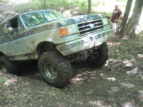 1991 Ford Bronco - This SUV is navigating a challenging off-road trail, with one wheel deep in a rut.