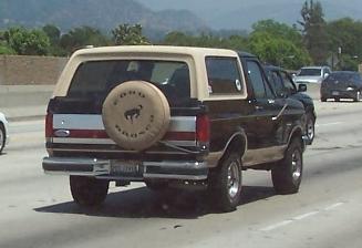 1990 Ford Bronco - Rear view of a Ford Bronco with a spare tire mounted on the back, seen on a highway.
