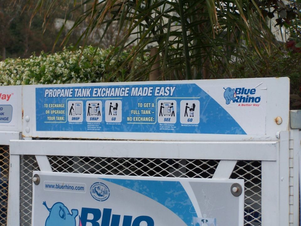 Sign explaining how to exchange propane tanks with Blue Rhino. Shows steps like drop, swap, go, see