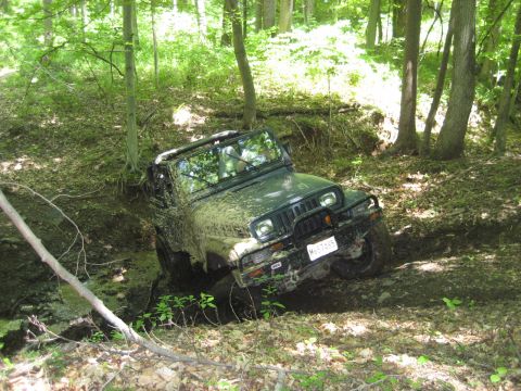1991 Ford Bronco - Jeep Wrangler stuck in mud on a wooded trail, license plate MHT7845 visible.