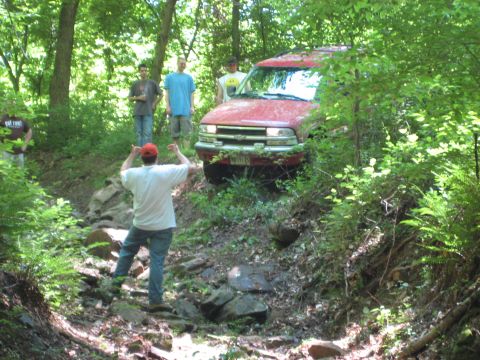 1991 Ford Bronco - A red Chevrolet Blazer S-10 is driven off-road on a rocky, wooded path.