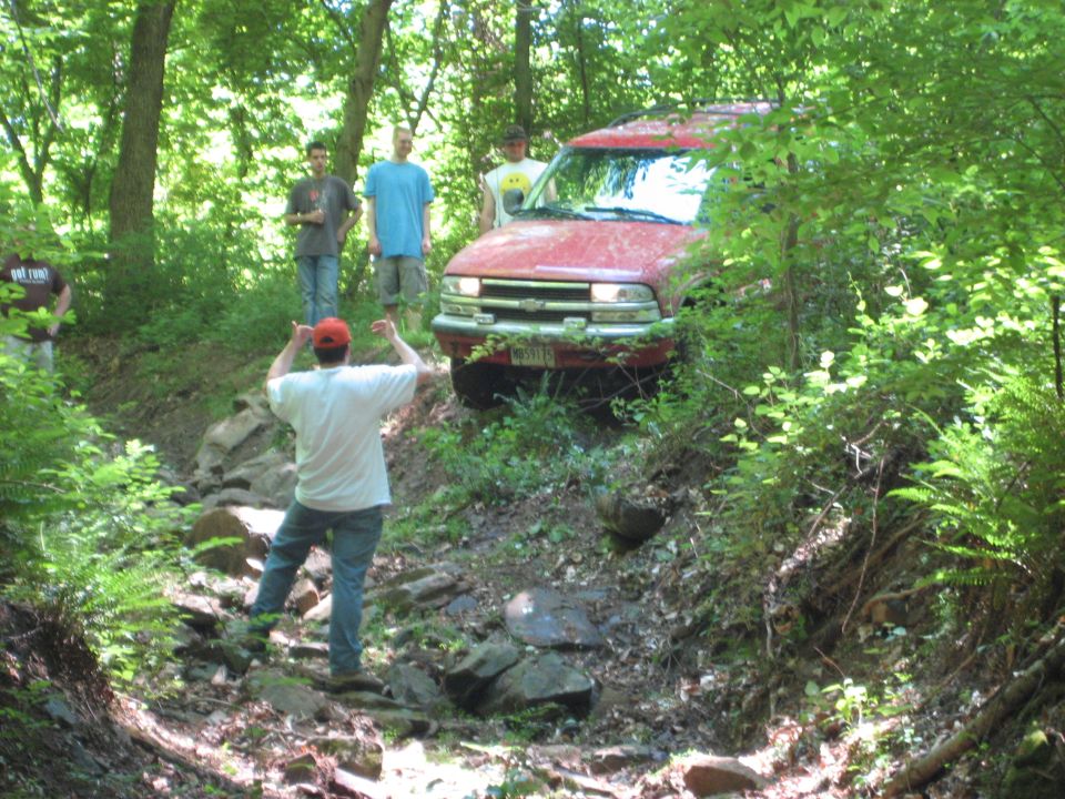 Red Chevrolet Blazer S-10 navigating a rocky, wooded trail with people watching