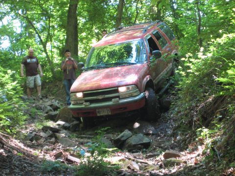 1991 Ford Bronco - A red SUV tackles a challenging off-road course through a dense forest.