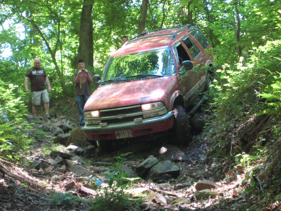 Red SUV navigating a rocky, wooded trail