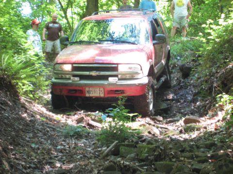 1991 Ford Bronco - A red SUV navigates a difficult off-road trail with onlookers present.