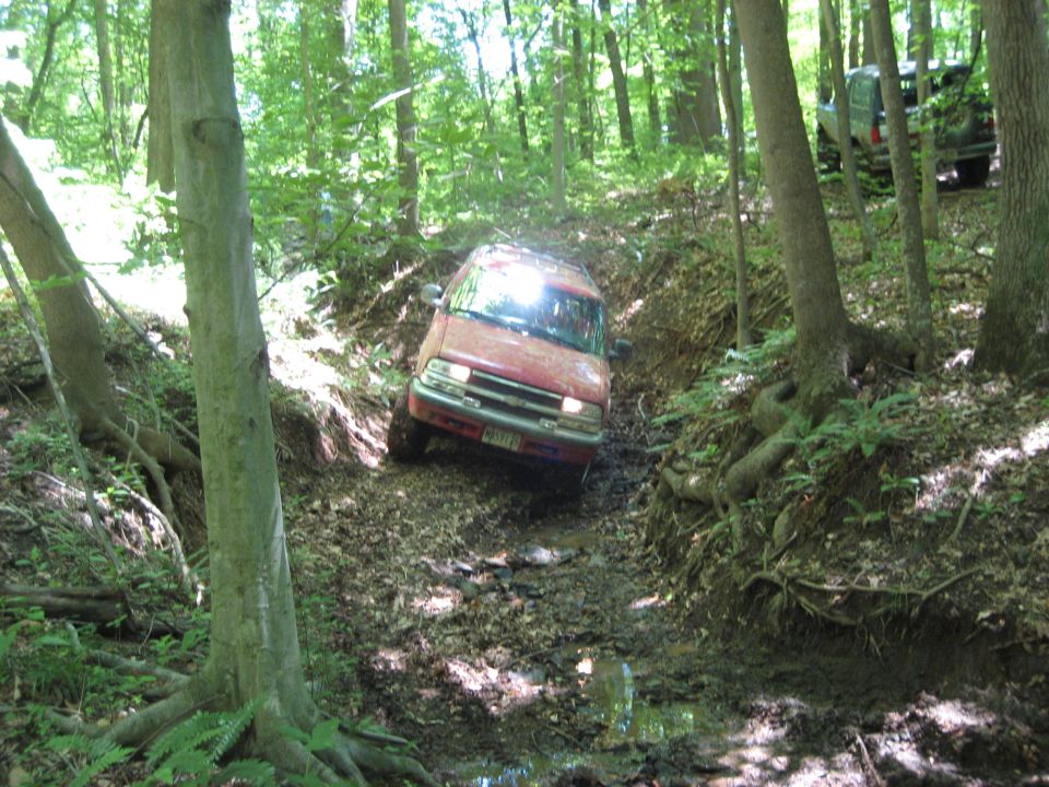 Red SUV navigating a muddy off-road trail; another vehicle visible in background