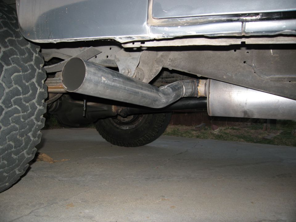 Exhaust pipe and muffler on a vehicle's underside, with a large tire visible