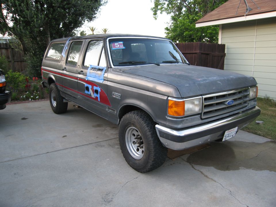 Gray 1986 Ford Bronco SUV with red stripe detail and blue tape on driver's door