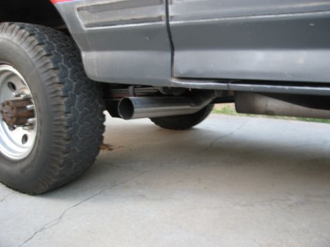 1986 Ford Bronco - A close-up view of the exhaust system and rear tire of a vehicle.