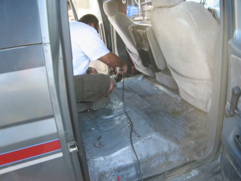 1986 Ford Bronco - A person works on the bare floor of a vehicle's interior, with seats visible.