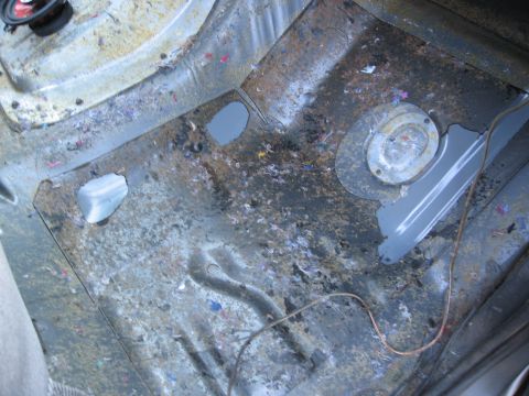 1986 Ford Bronco - The interior floor of a vehicle, showing exposed metal, debris, and wiring, suggesting a stripped-down or disassembled state.