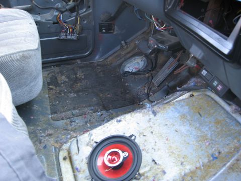 1986 Ford Bronco - The interior floor of a vehicle is shown with exposed wiring and a speaker removed from its mounting.