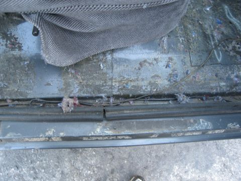 1986 Ford Bronco - The interior floor of a vehicle shows accumulated dirt, debris, and wiring beneath the seat.