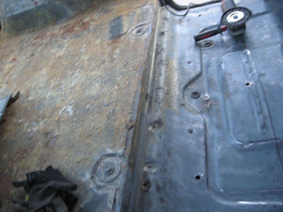 Vehicle floor being prepped with a grinder, showing rust and metal