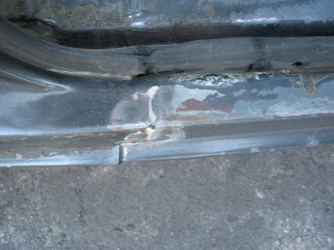 1986 Ford Bronco - The door sill shows signs of rust and damage, with a black rubber seal visible above it.