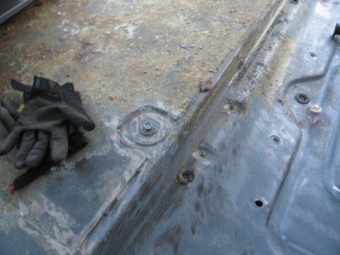 1986 Ford Bronco - Close-up of a vehicle's interior floor pan, showing dirt, bolts, and signs of wear.