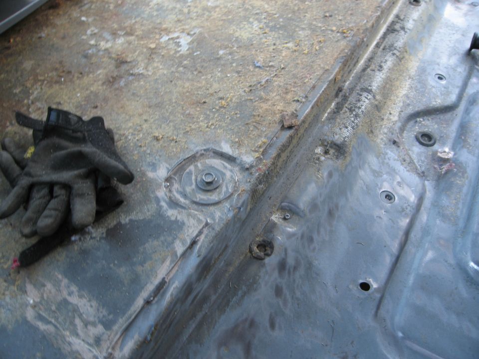 Gloves on dirty metal floor pan with bolts and some rust