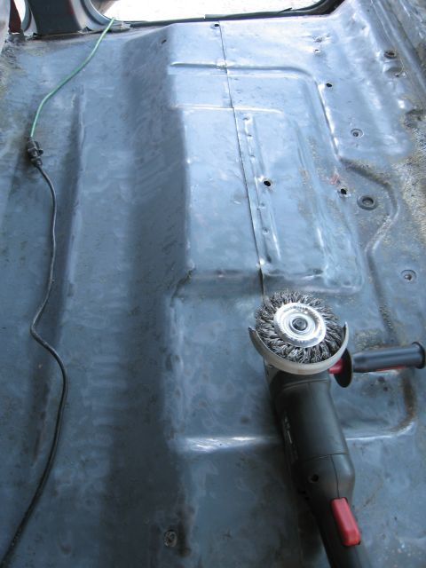 1986 Ford Bronco - A wire wheel grinder is positioned on the gray floor pan of a vehicle, with a green wire visible.