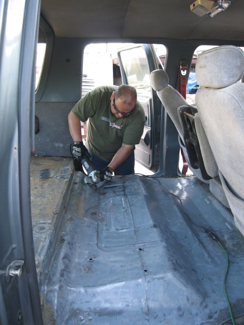 1986 Ford Bronco - A person uses an angle grinder on the interior floor of a vehicle, likely during restoration or repair.
