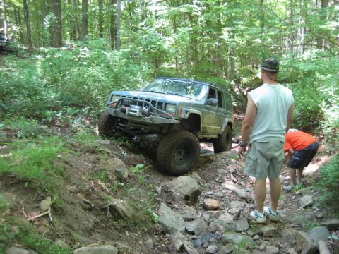 1991 Ford Bronco - Modified Jeep Cherokee XJ navigating a challenging off-road course in a wooded area.