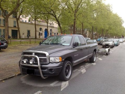 1991 Ford Crown Victoria - A gray Dodge Ram pickup truck with a front bull bar and auxiliary lights is seen towing a trailer on a tree-lined street.