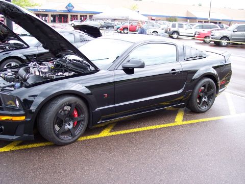1972 Ford Ranchero - A black coupe with its hood open, revealing the engine, is parked in a lot with other vehicles.