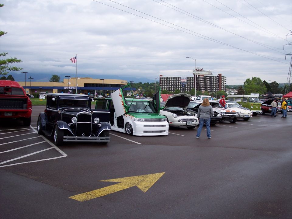 Modified Scion xB with green flames and gullwing doors parked next to a classic car and a red pickup truck