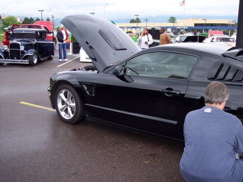 1972 Ford Ranchero - A black coupe with its hood open is parked on a wet asphalt lot next to other vehicles.